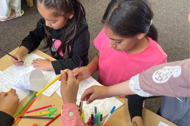 Two children sat at a table drawing and colouring